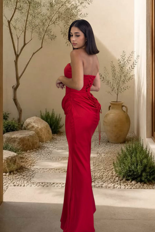 Woman in a red strapless gown standing in an outdoor setting with plants and rocks.