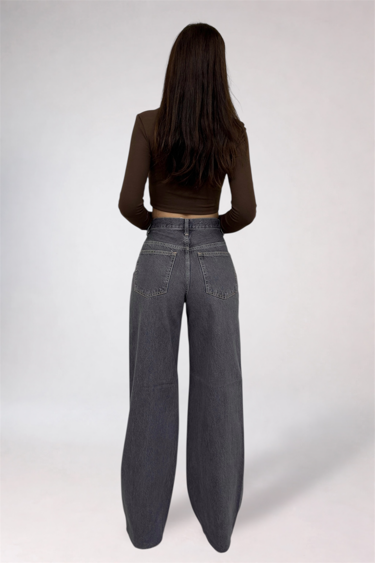 Person wearing a brown top and gray wide-leg jeans on a white background