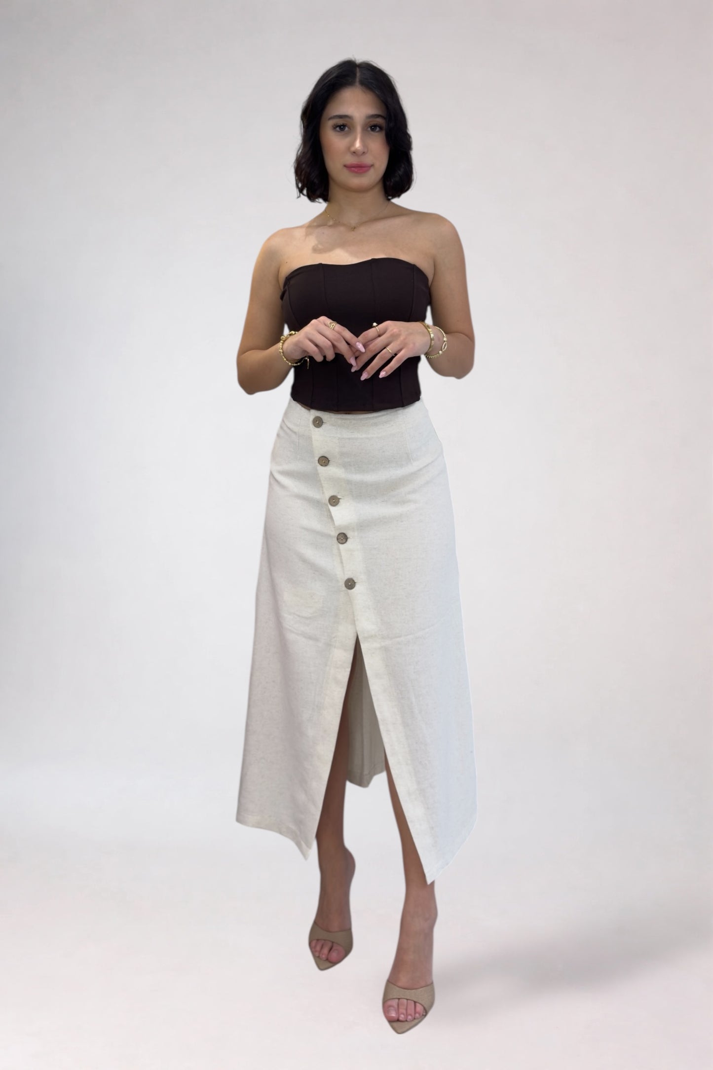 Woman wearing a black strapless top and white button-up skirt on a plain background