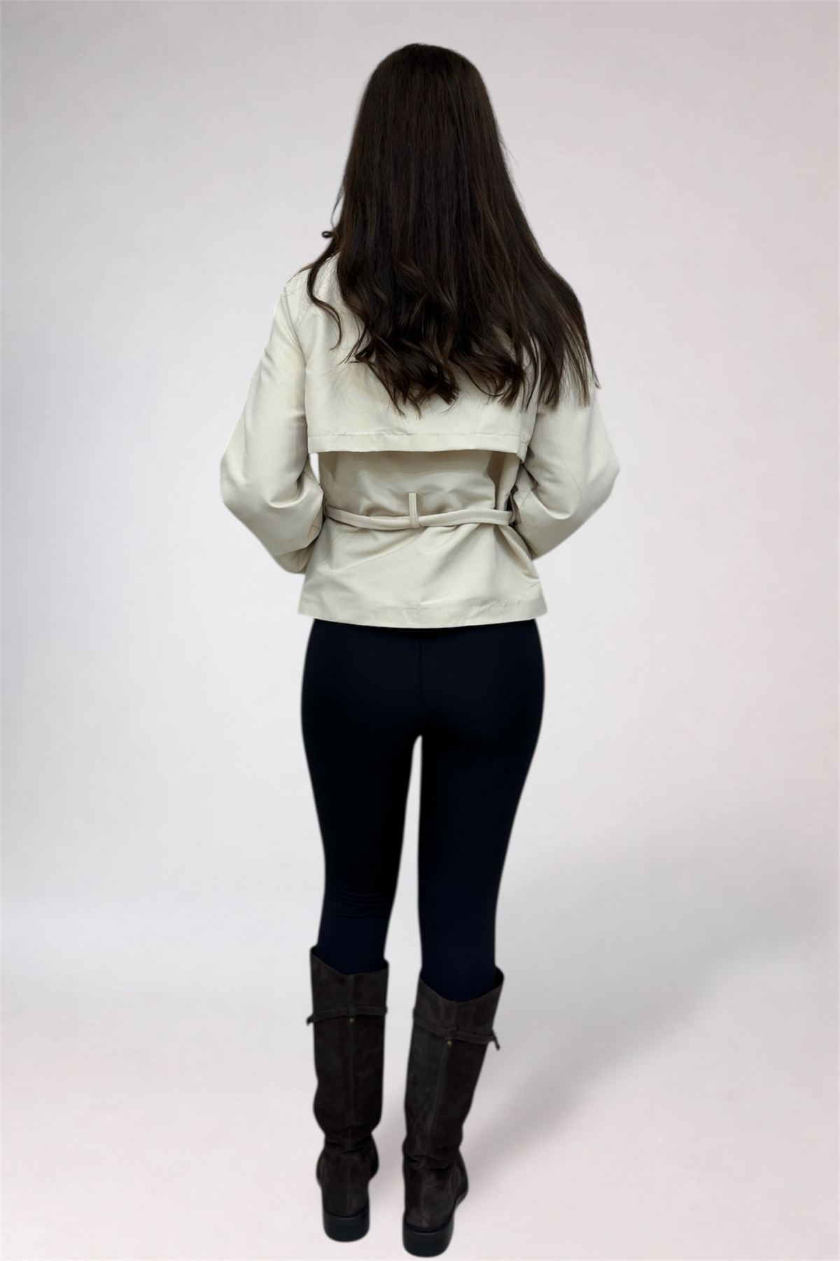 Person wearing a light-colored jacket, dark pants, and black boots on a white background