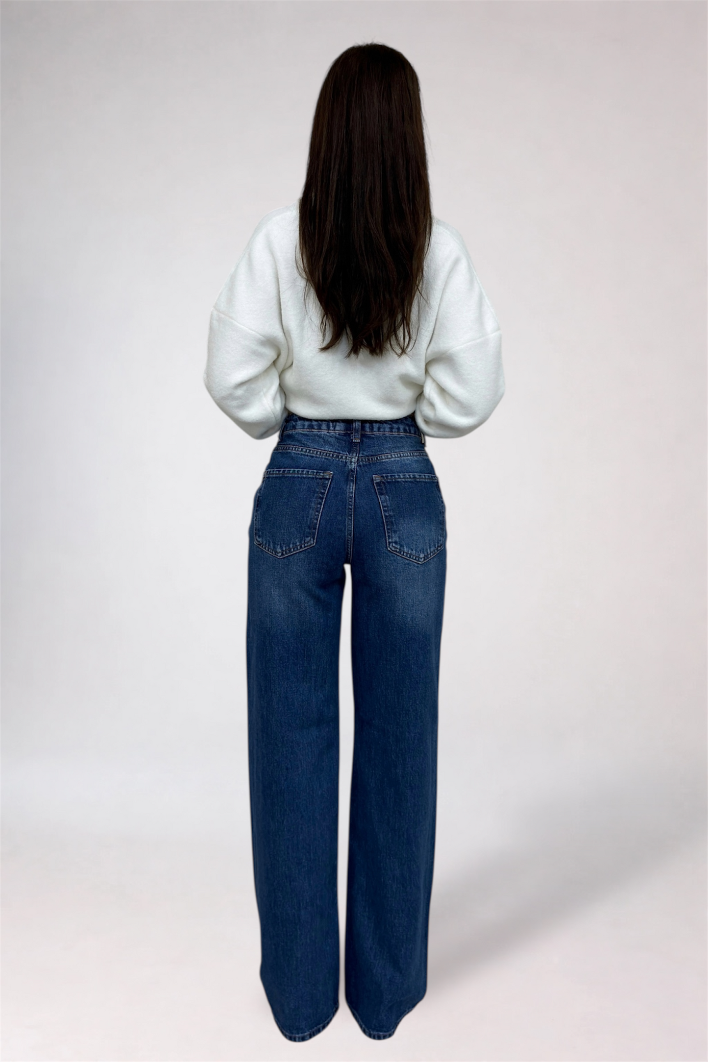 Person wearing blue jeans and a white top on a plain background