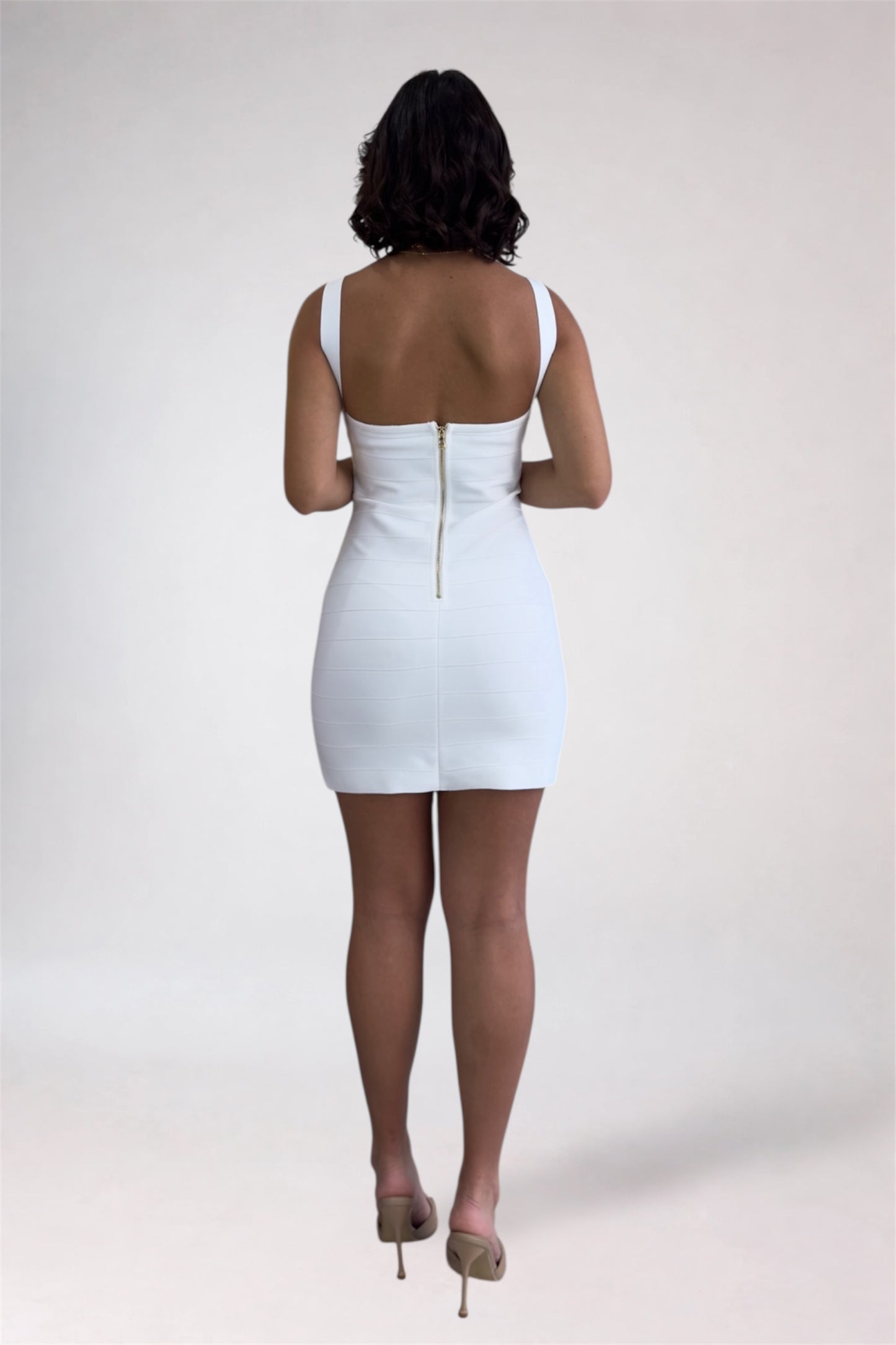 Person wearing a white dress with a gold zipper on a plain background