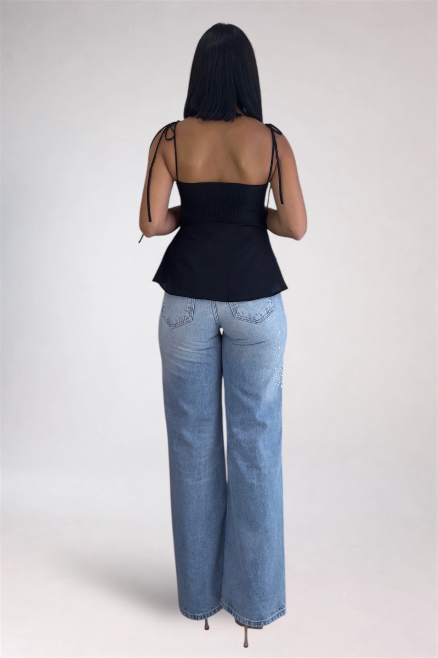 Person wearing a black top and blue jeans on a white background