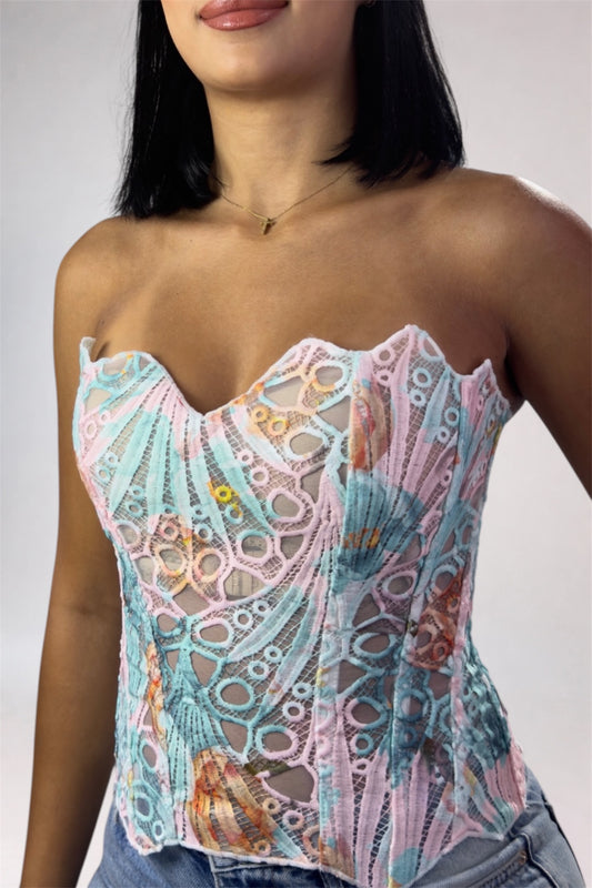 Woman wearing a colorful lace corset top against a plain background