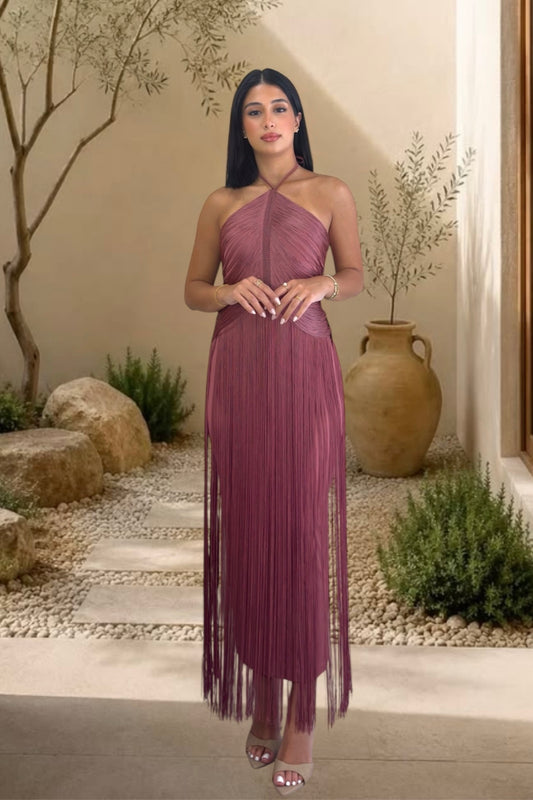 Woman in a purple one-shoulder dress standing in an outdoor setting with plants and stones.