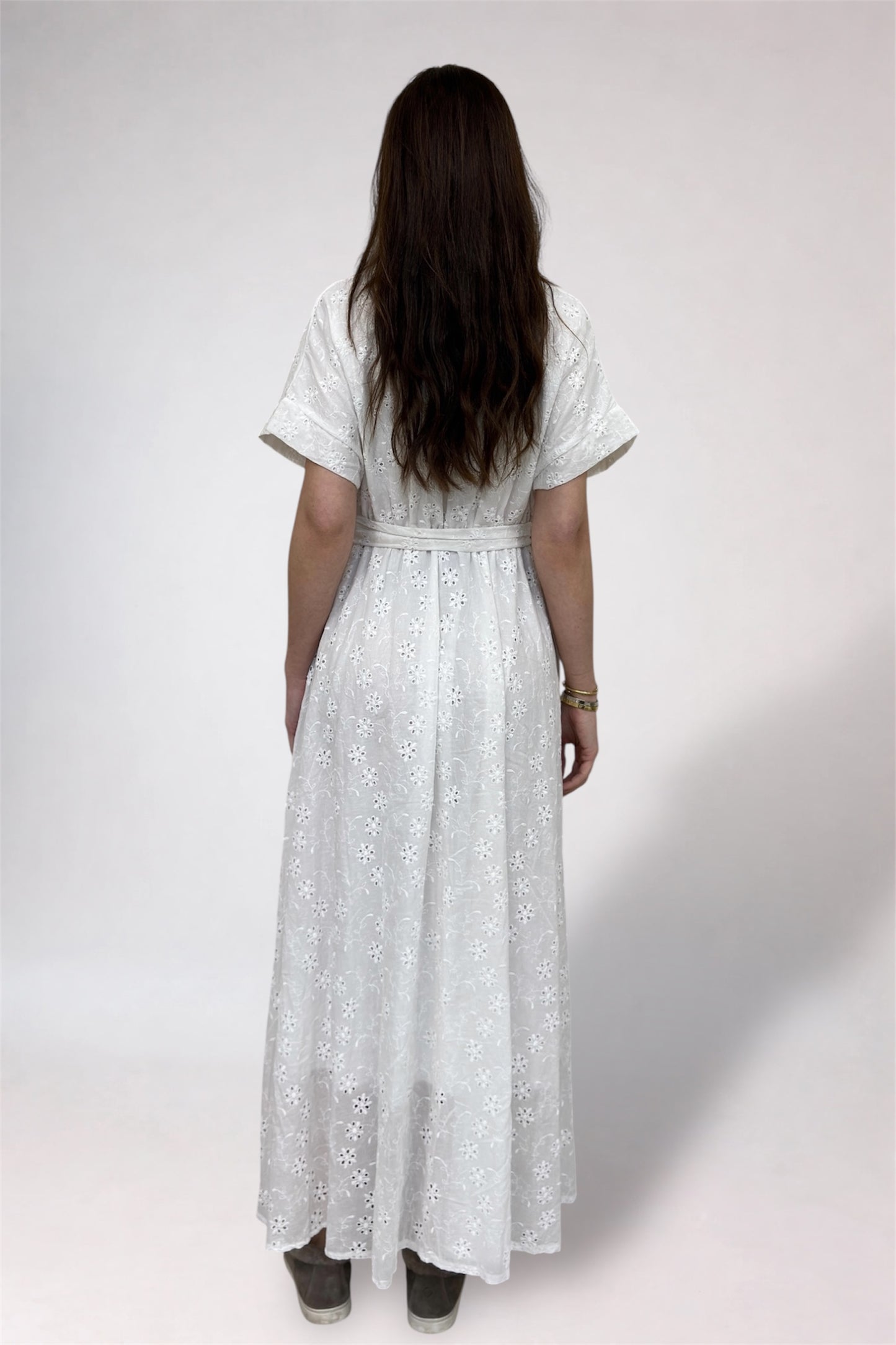 Woman wearing a white lace dress from behind on a plain background
