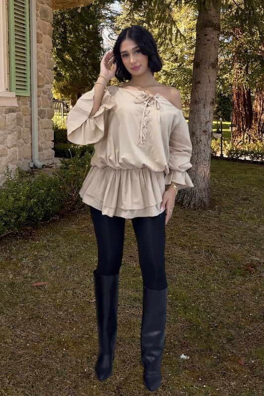 Woman wearing a beige off-shoulder blouse and black leggings outdoors.