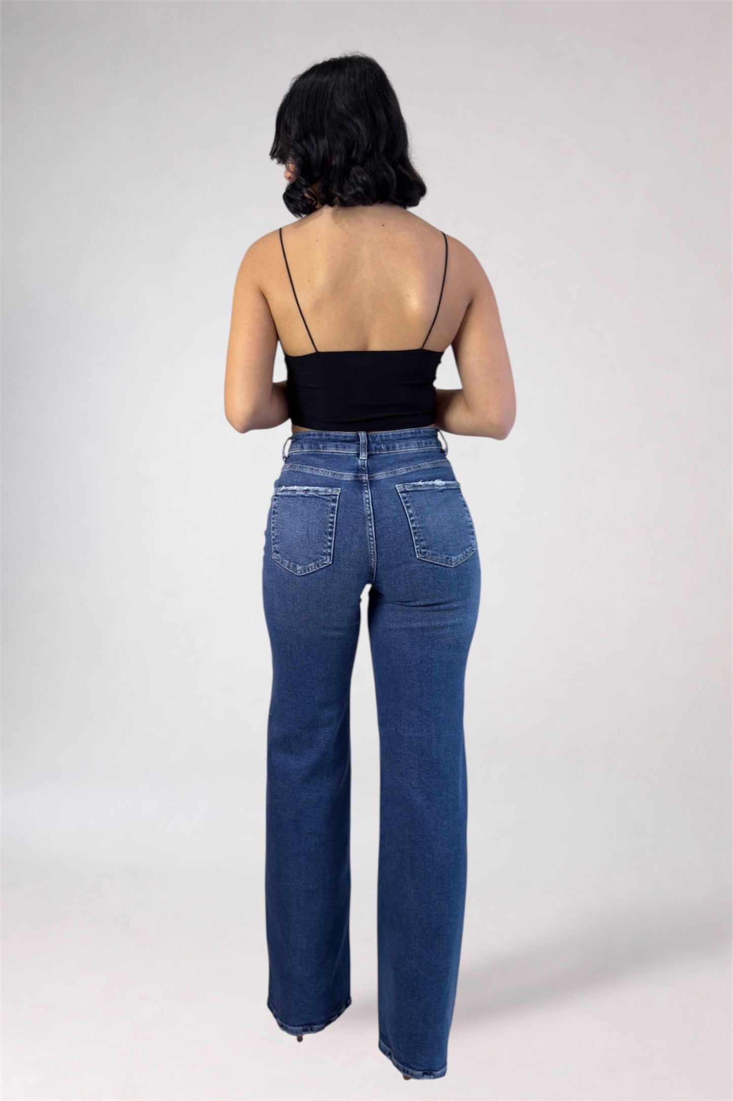 Person wearing blue jeans and a black top on a plain background
