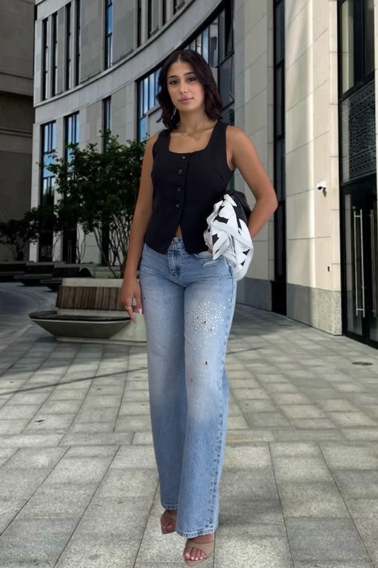 Woman in black sleeveless top and blue jeans standing on a city street.