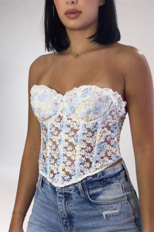 Woman wearing a floral strapless top and jeans against a plain background