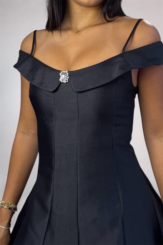 A close-up of a woman wearing a dark navy off-the-shoulder dress with a structured collar and a sparkling rhinestone brooch at the neckline.