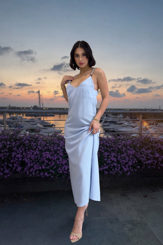 Woman in a light blue dress standing on a rooftop with a sunset view over water.