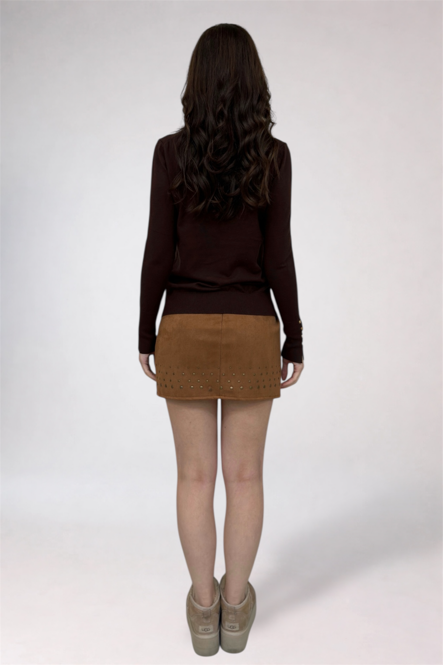 Person wearing a brown sweater and tan skirt on a white background