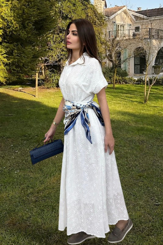 Woman in a white dress with a blue ribbon standing in a garden.