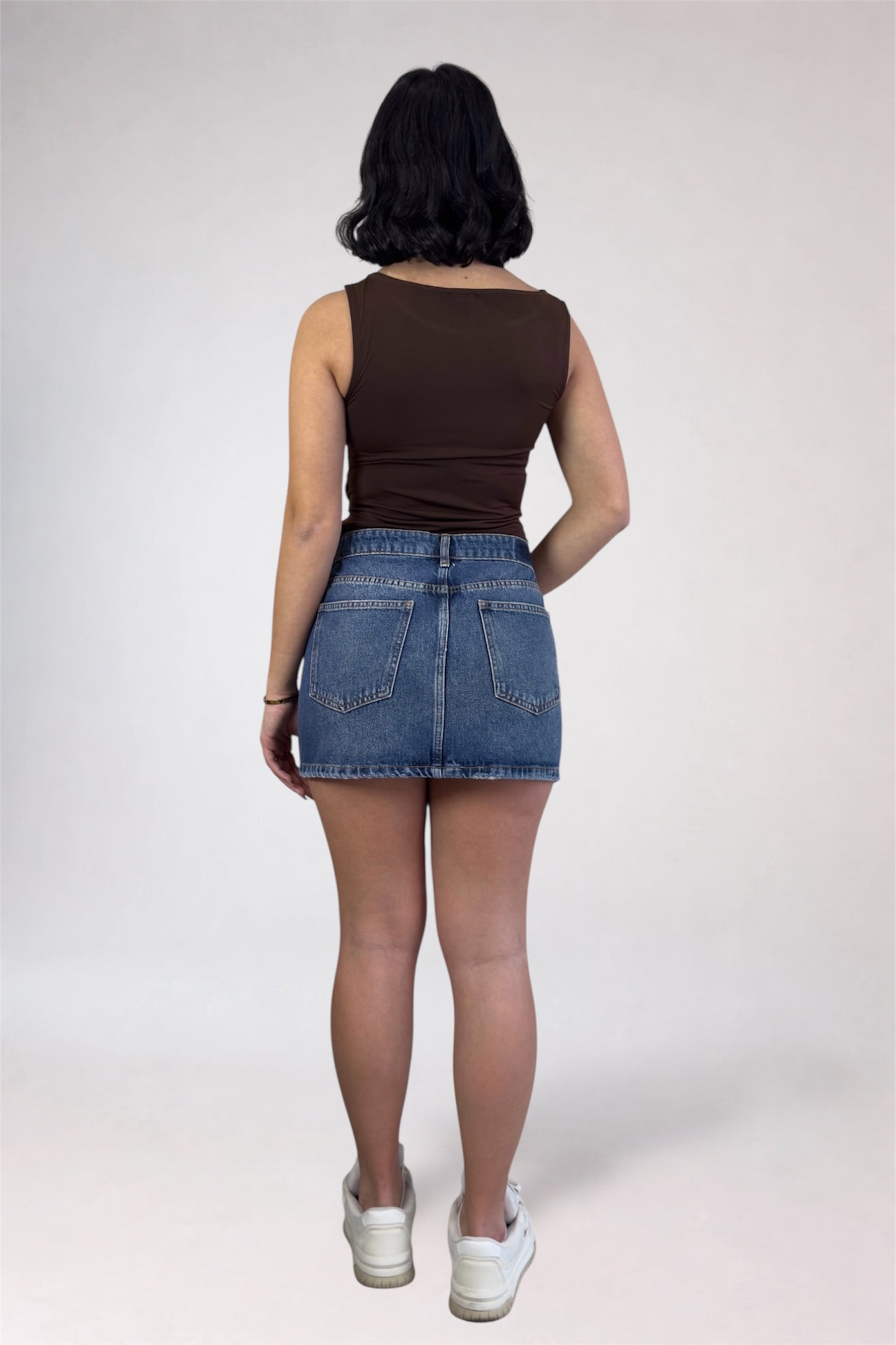 Person wearing a brown tank top and denim skirt on a white background