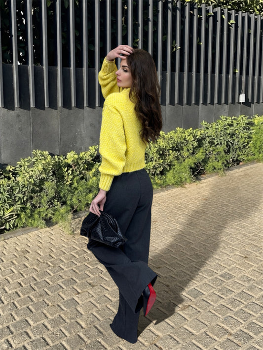 Woman in a yellow sweater and black pants walking outdoors on a paved path.