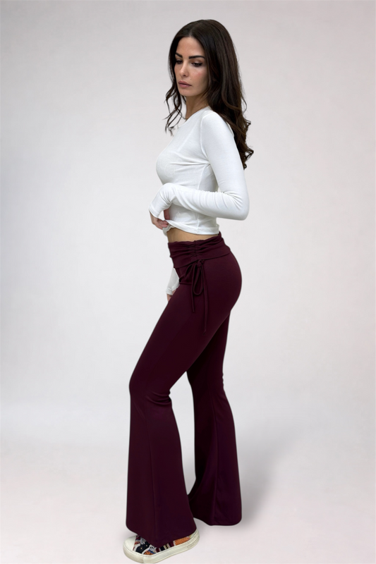 Woman wearing a white long-sleeve top and dark purple flared pants on a plain background