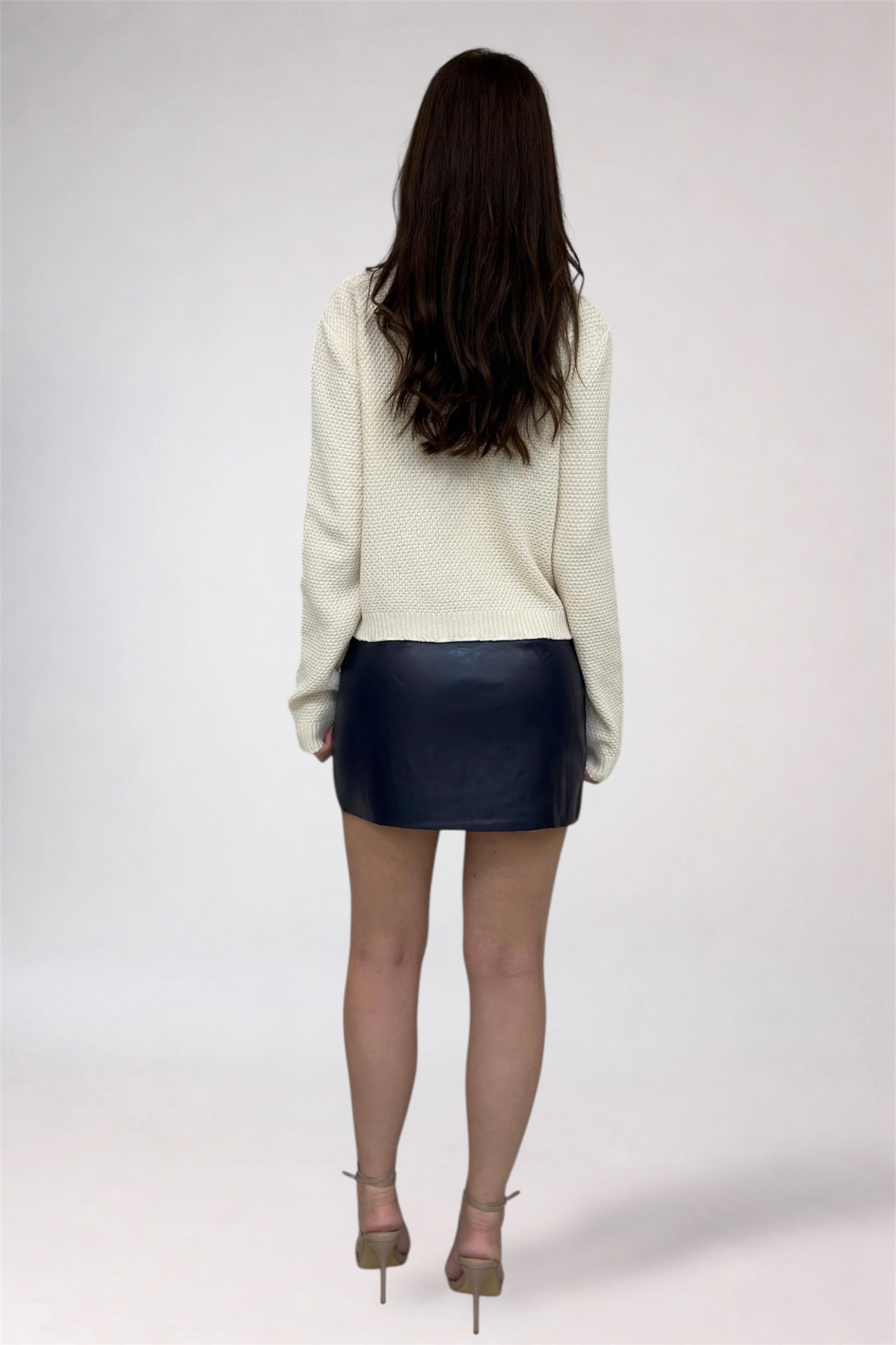 Person wearing a cream sweater and black leather skirt on a white background