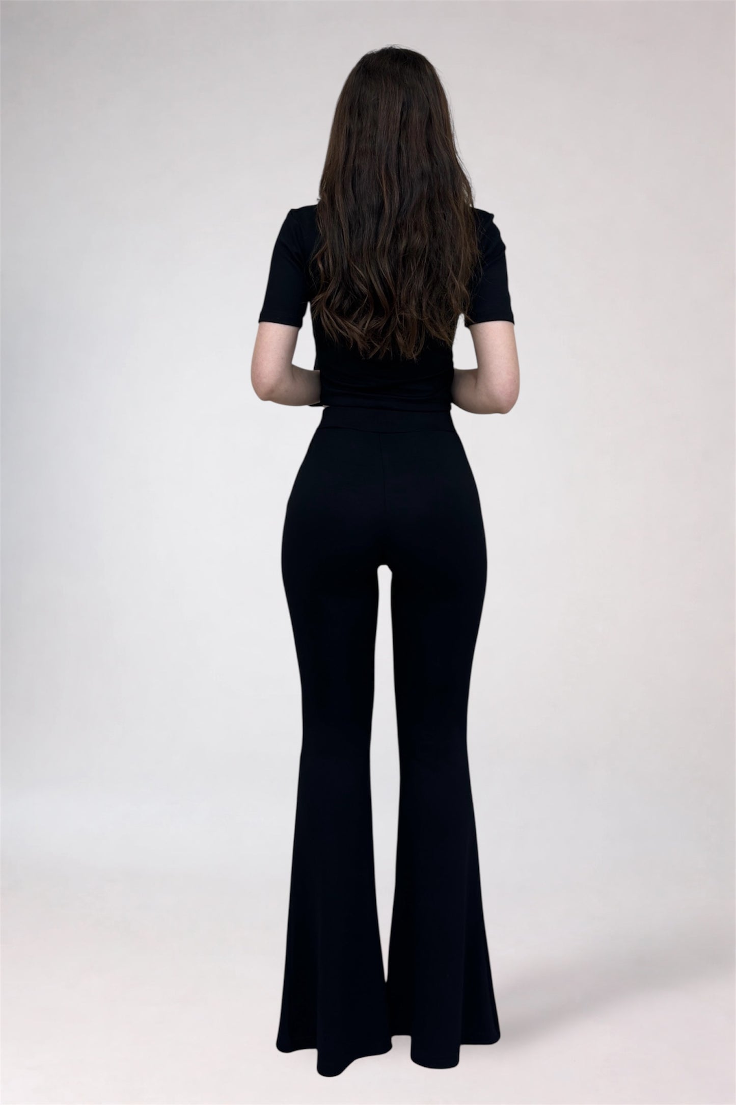 Person wearing a black outfit with flared pants on a white background