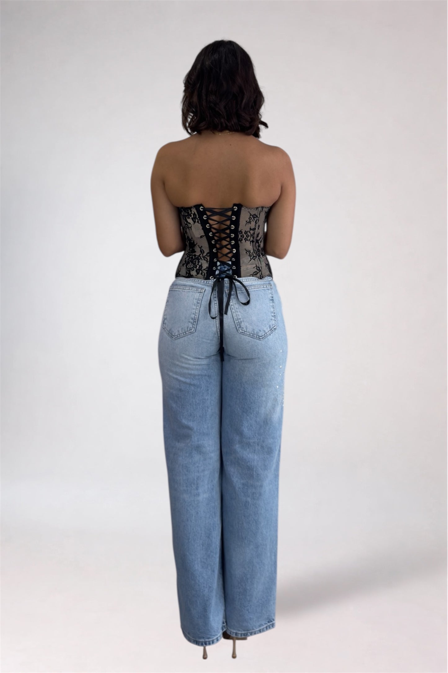 Person wearing a black lace corset and blue jeans on a white background