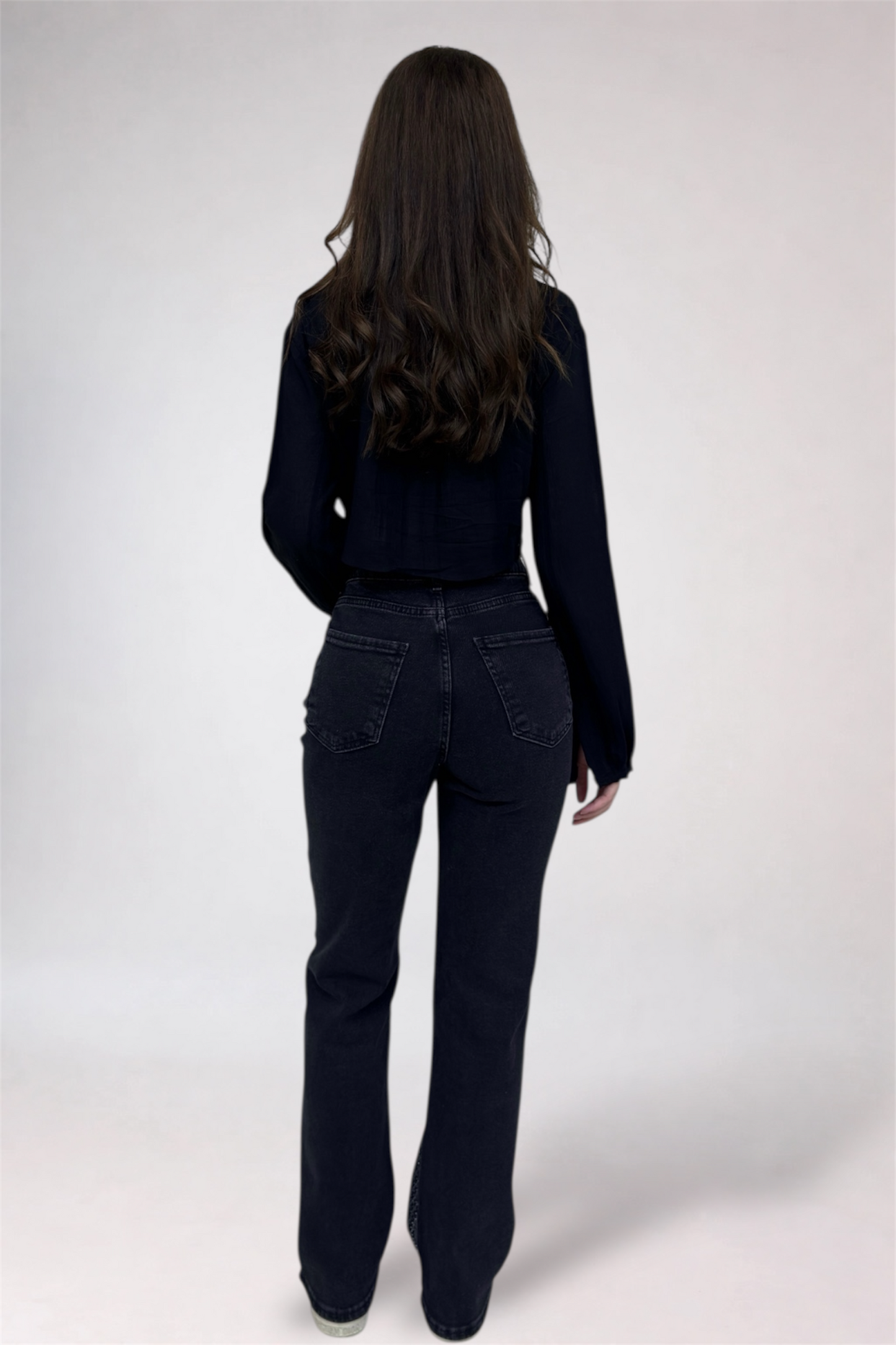 Person wearing a black outfit with flared jeans on a white background