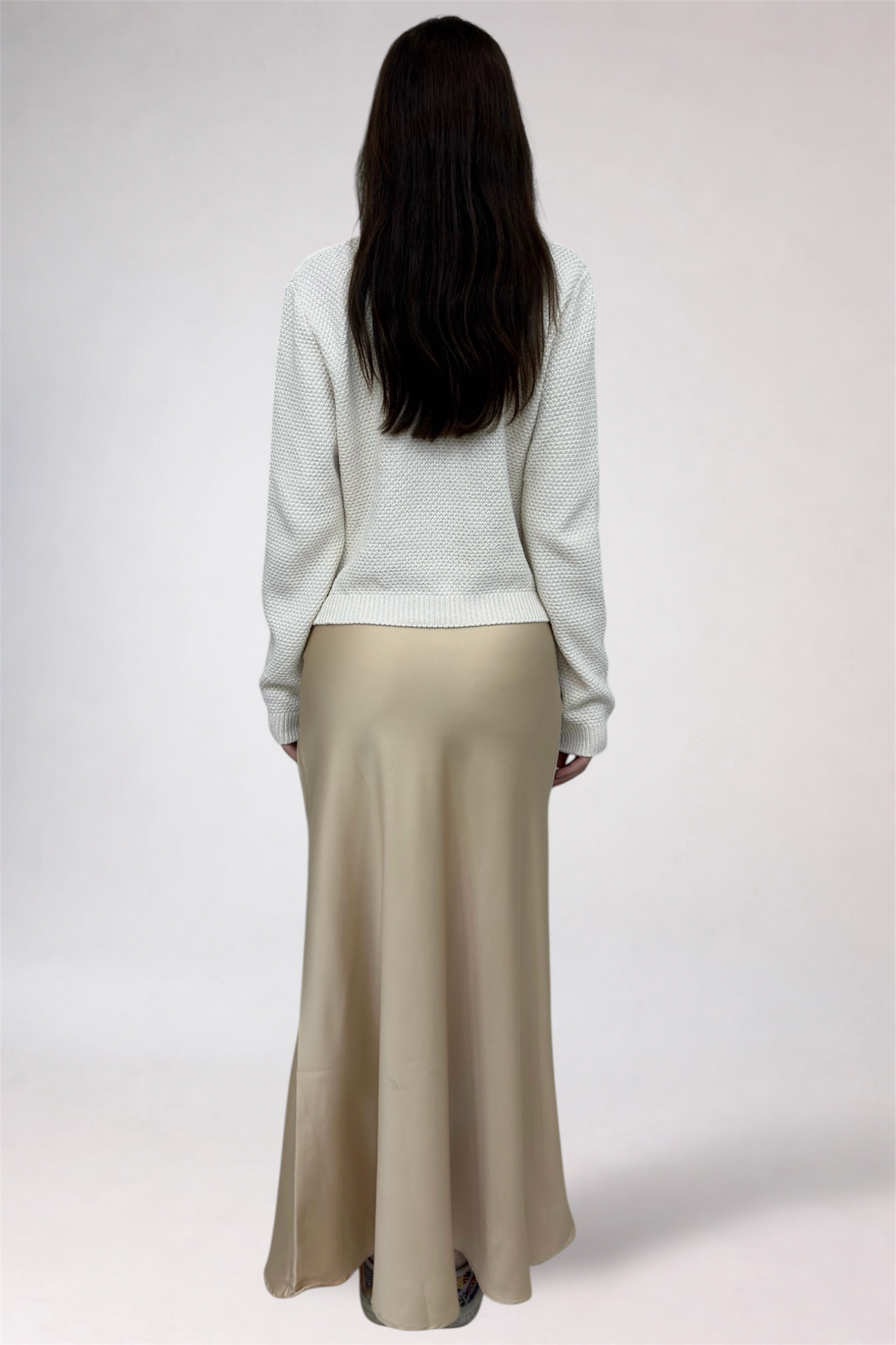 Person wearing a white sweater and beige skirt on a plain background