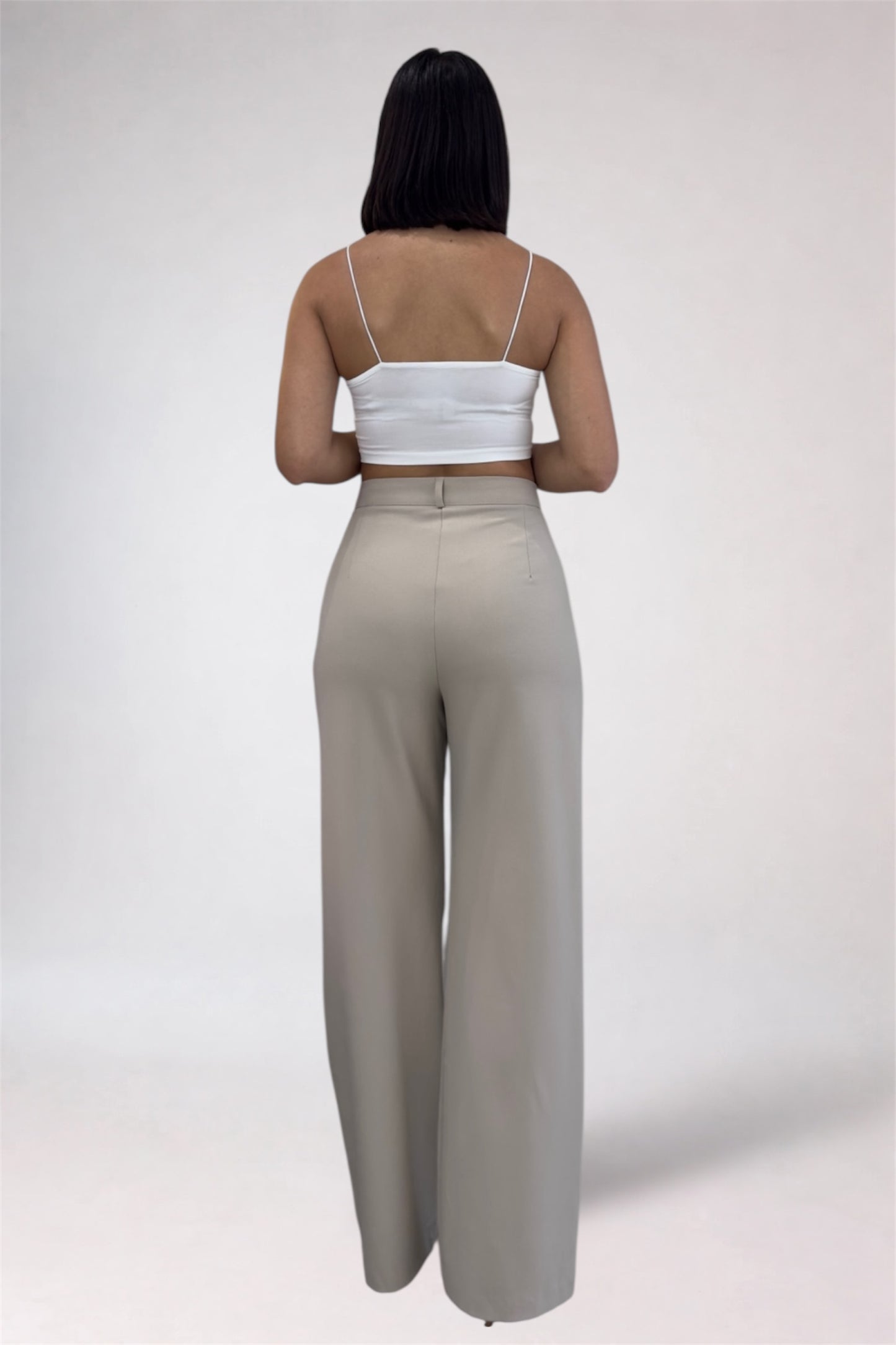 Woman wearing a white top and beige high-waisted pants on a plain background