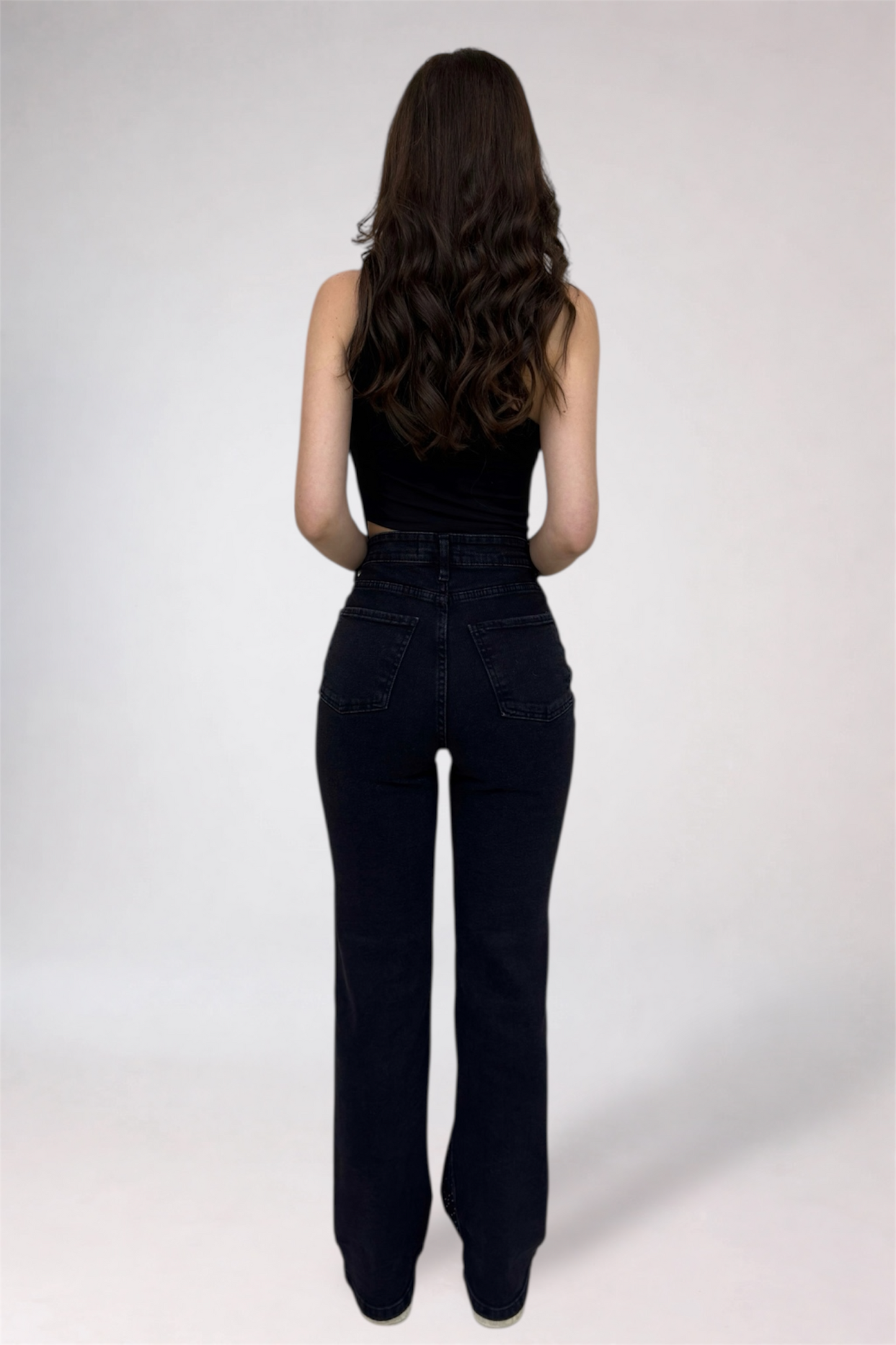 Person wearing black high-waisted jeans and a black top on a white background