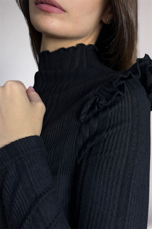 Close-up of a person wearing a black ribbed sweater with ruffled details.