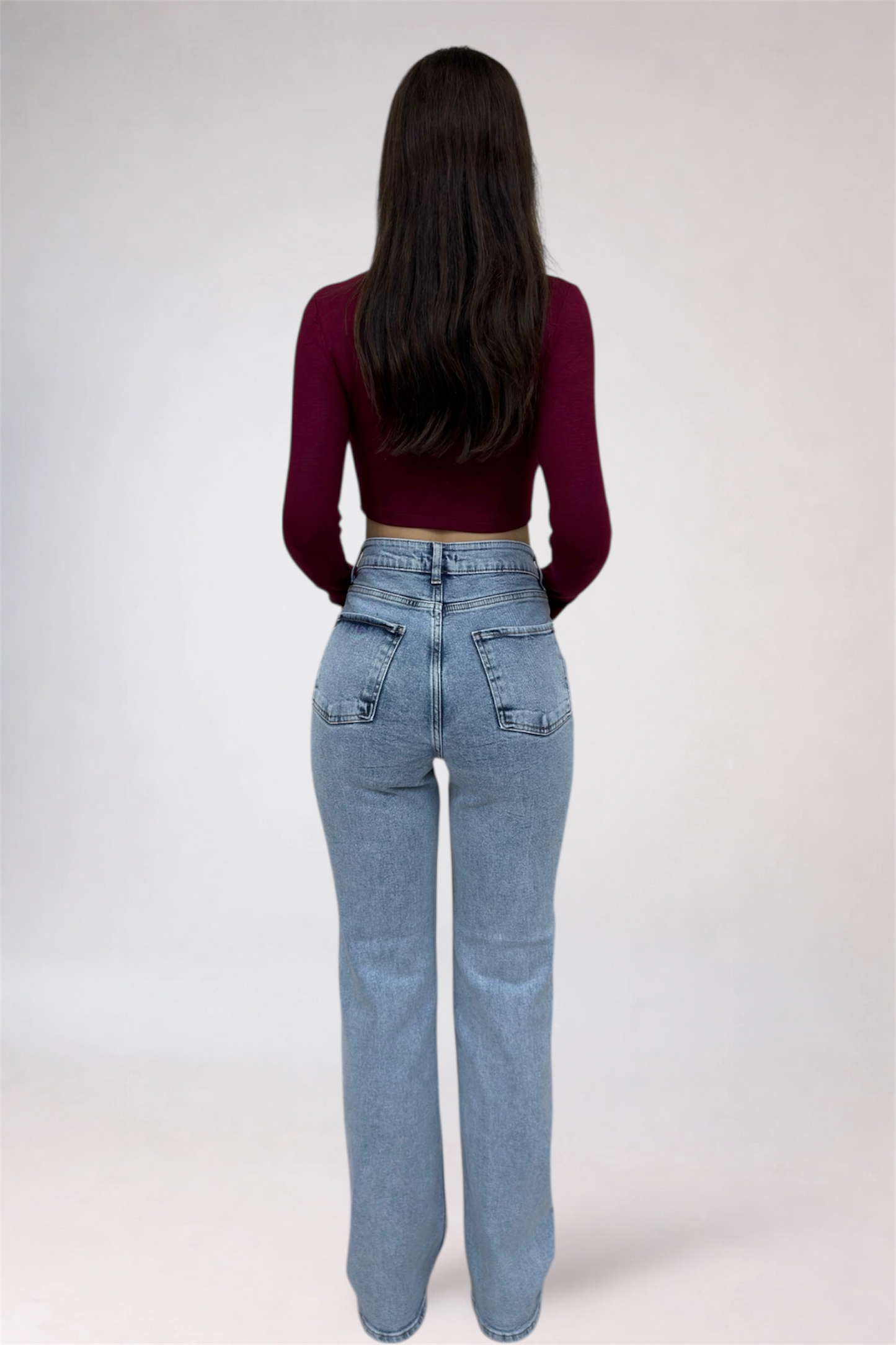 Person wearing a burgundy top and light blue jeans on a white background