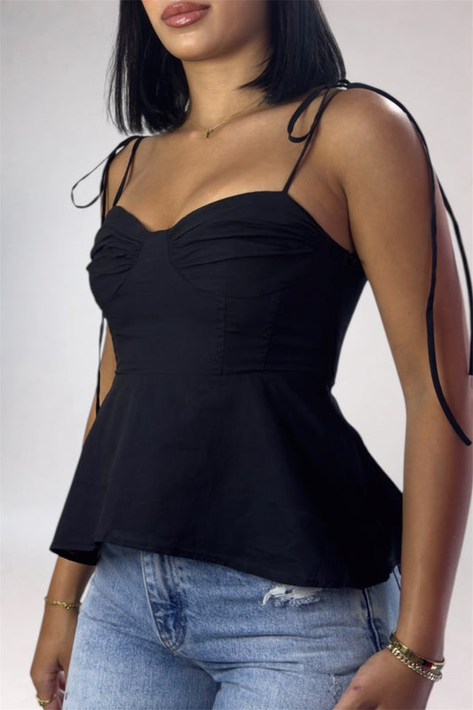 Black peplum top with thin straps worn by a model on a plain background