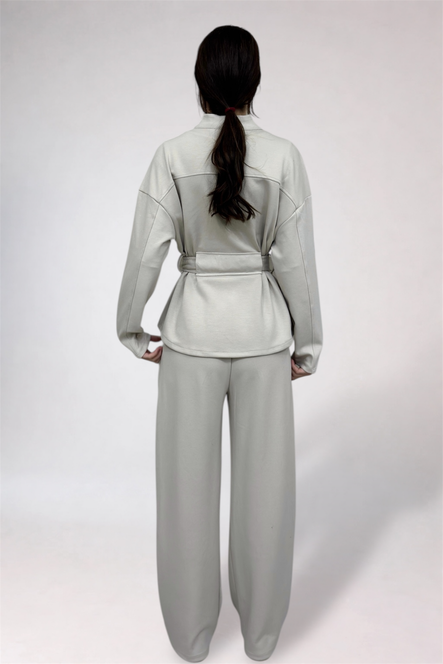 Person wearing a light gray outfit with a belt on a white background