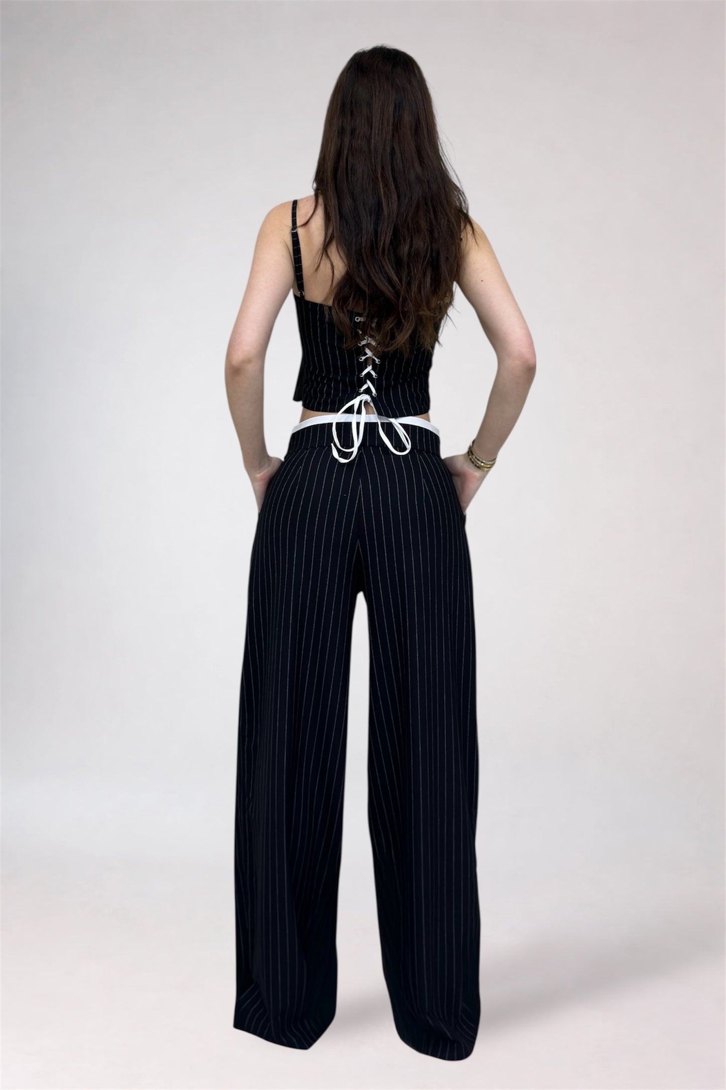 Woman wearing a black lace-up top and wide-leg pants on a white background