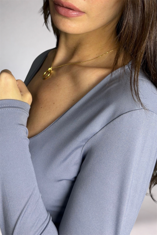 Close-up of a person wearing a light blue top and gold necklace against a neutral background