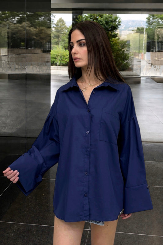 Woman wearing a blue shirt standing in an outdoor setting with trees and a building.