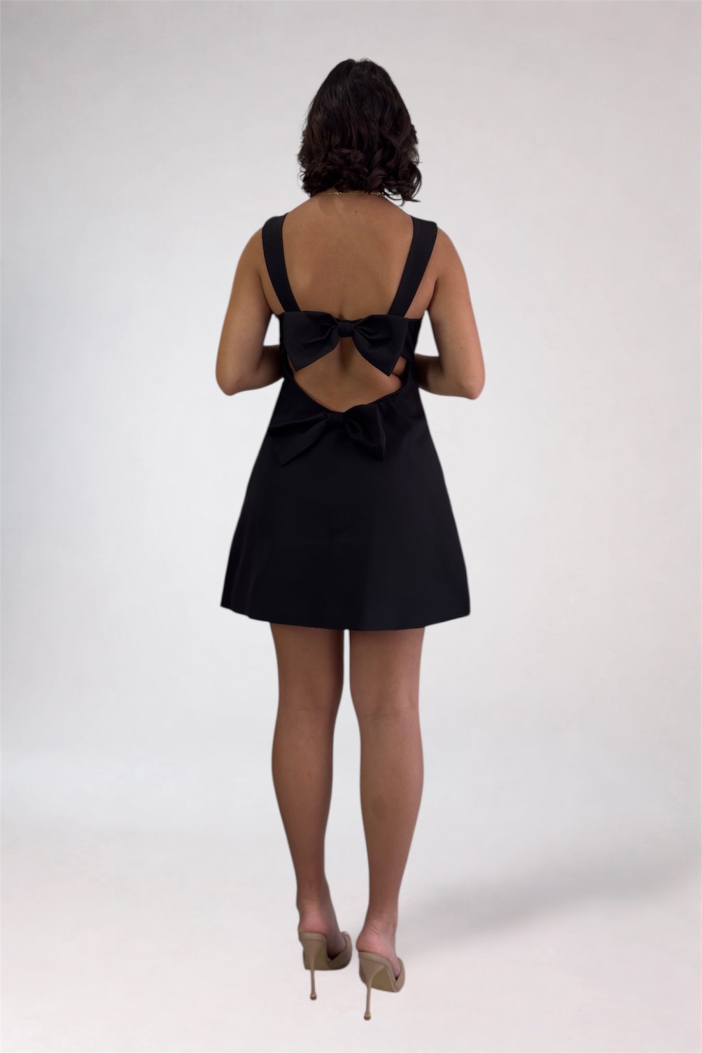 Black dress with a bow detail on the back worn by a person on a white background