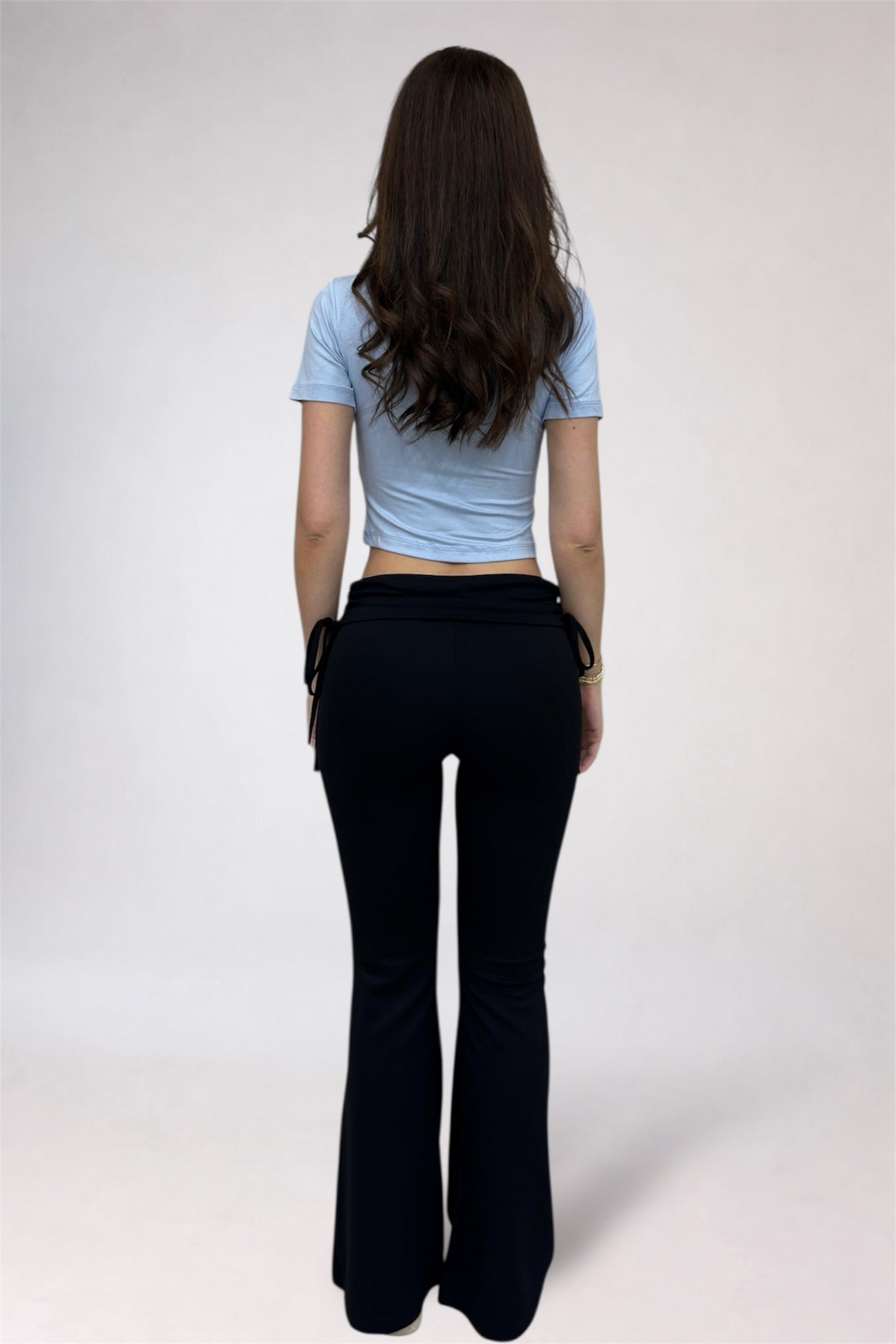 Person wearing a light blue crop top and black flared pants on a white background
