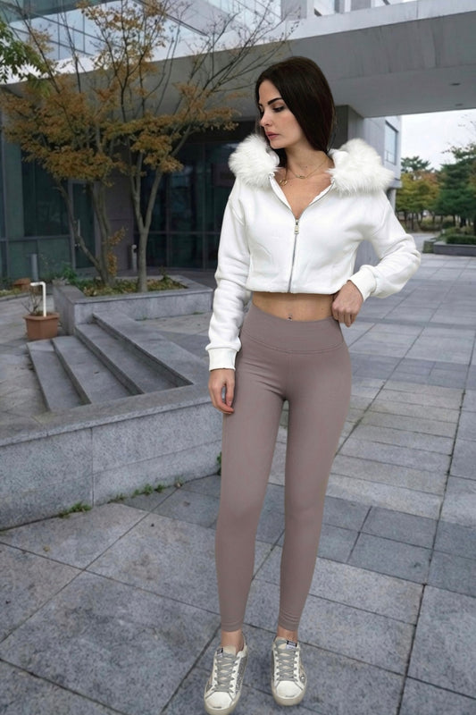Woman wearing a white cropped jacket with fur trim and beige leggings outdoors.