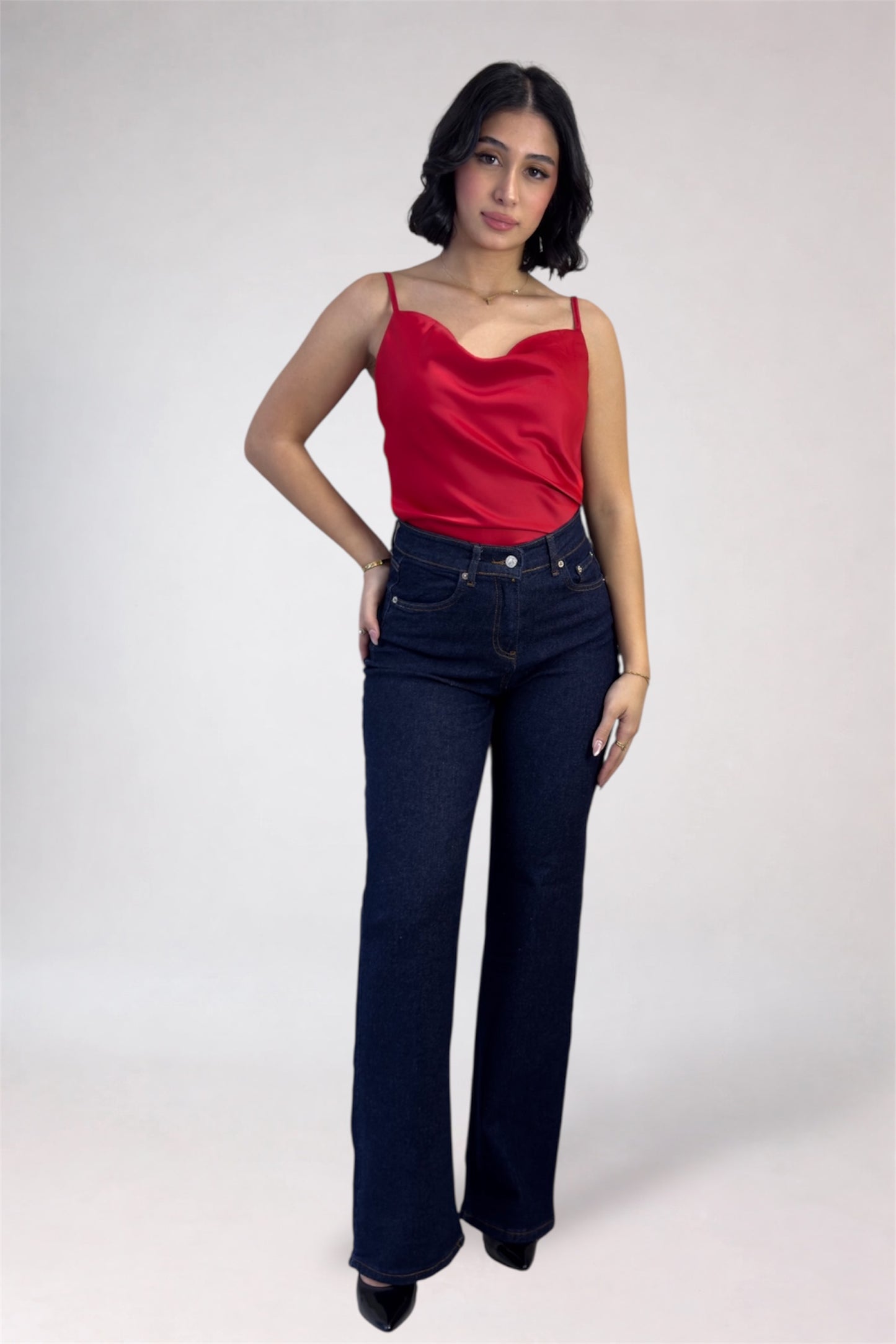 Woman wearing a red top and dark blue jeans on a white background