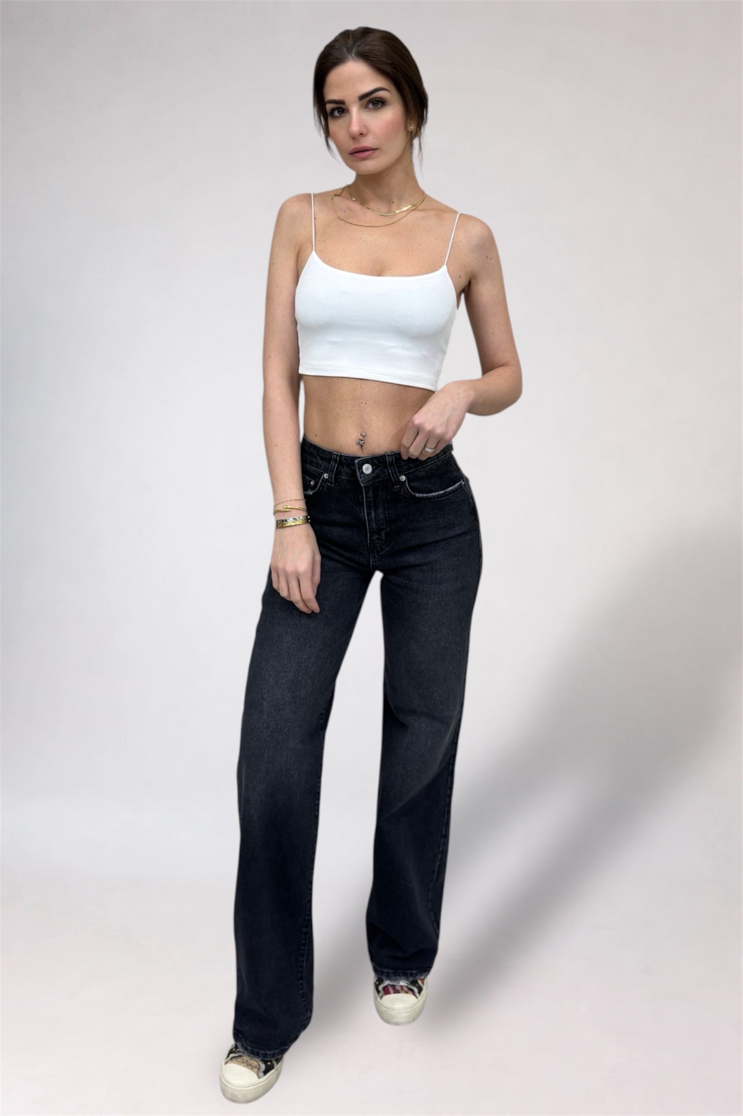 Woman wearing a white tank top and black jeans on a plain background