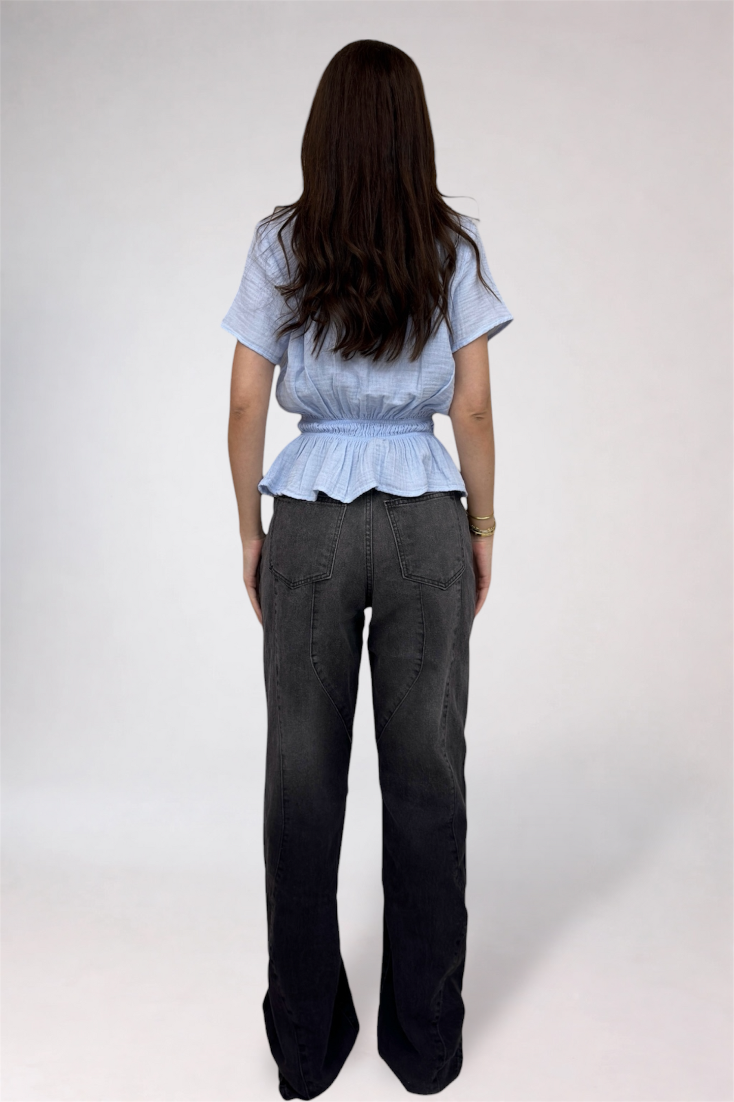 Person wearing a light blue top and dark gray pants on a white background