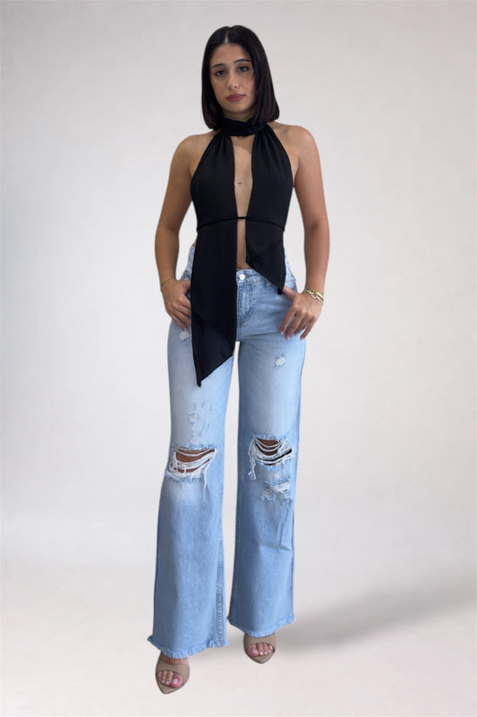 Woman wearing a black sleeveless top and light blue ripped jeans on a white background
