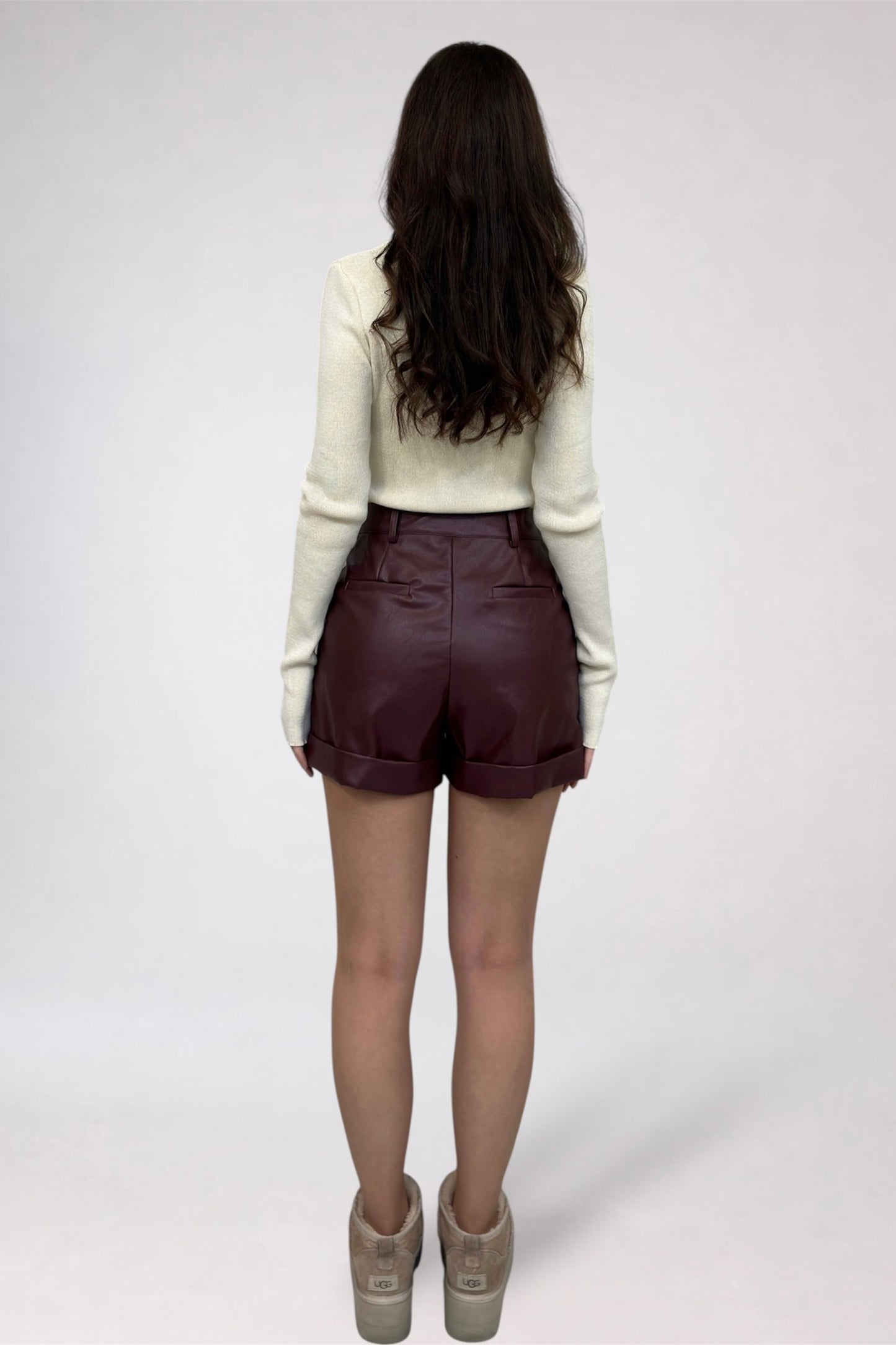 Person wearing brown leather shorts and a white sweater on a plain background
