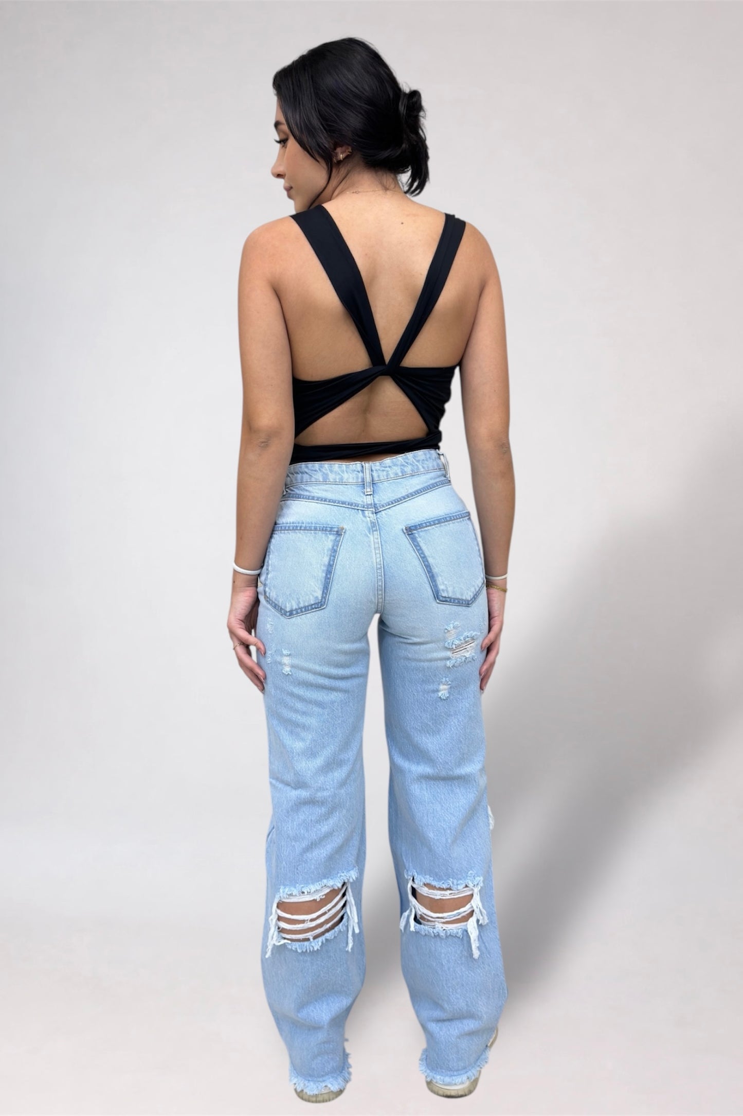 Person wearing a black strappy top and light blue ripped jeans on a plain background