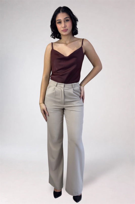 Woman wearing a brown top and beige pants against a white background