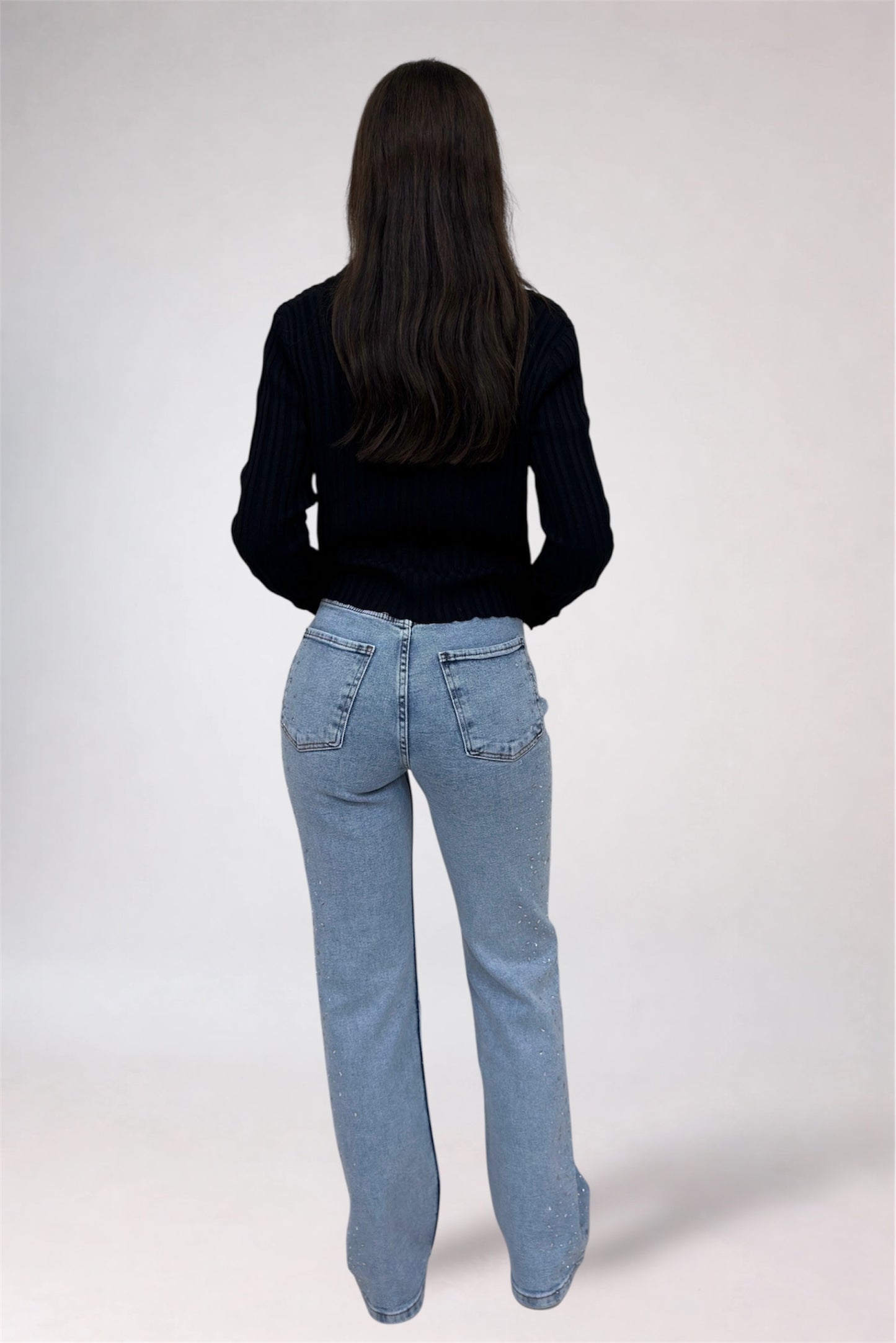 Person wearing a black top and light blue jeans on a white background