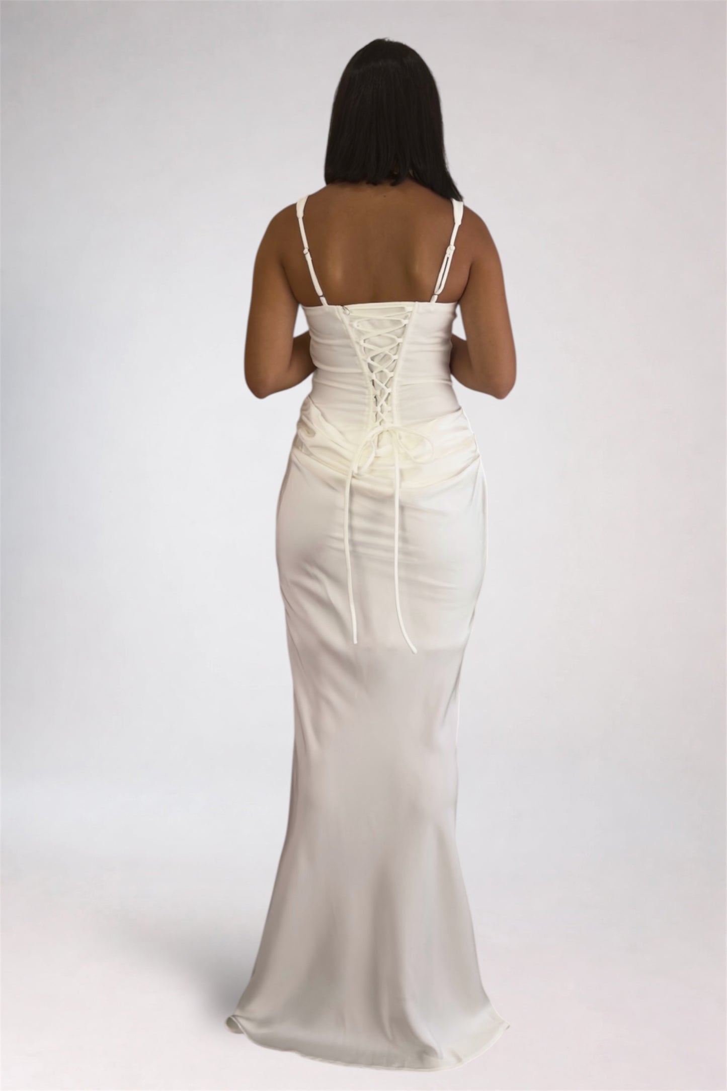 Woman wearing a white evening gown with thin straps on a plain background