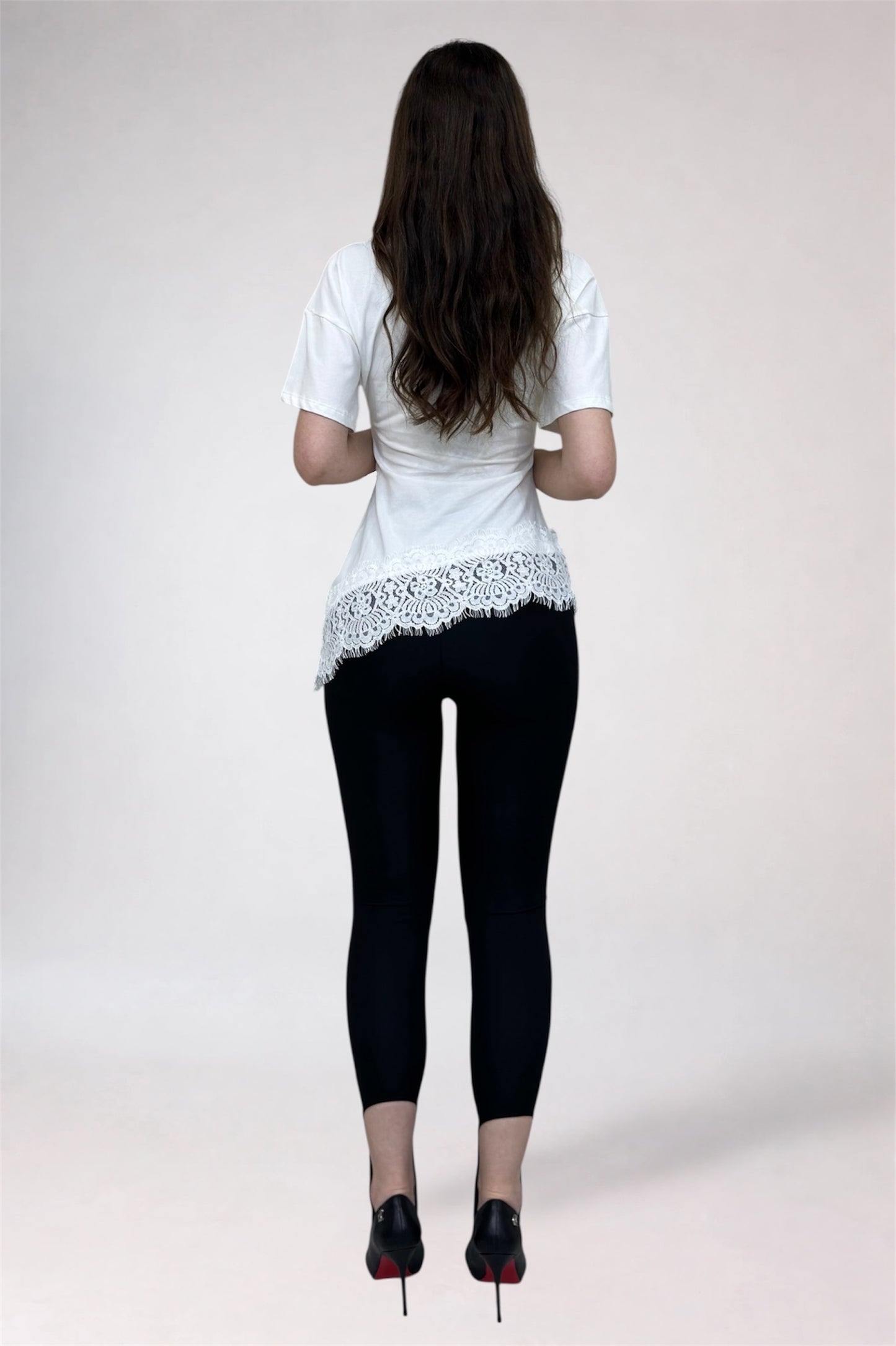 Person wearing a white lace top and black leggings on a plain background
