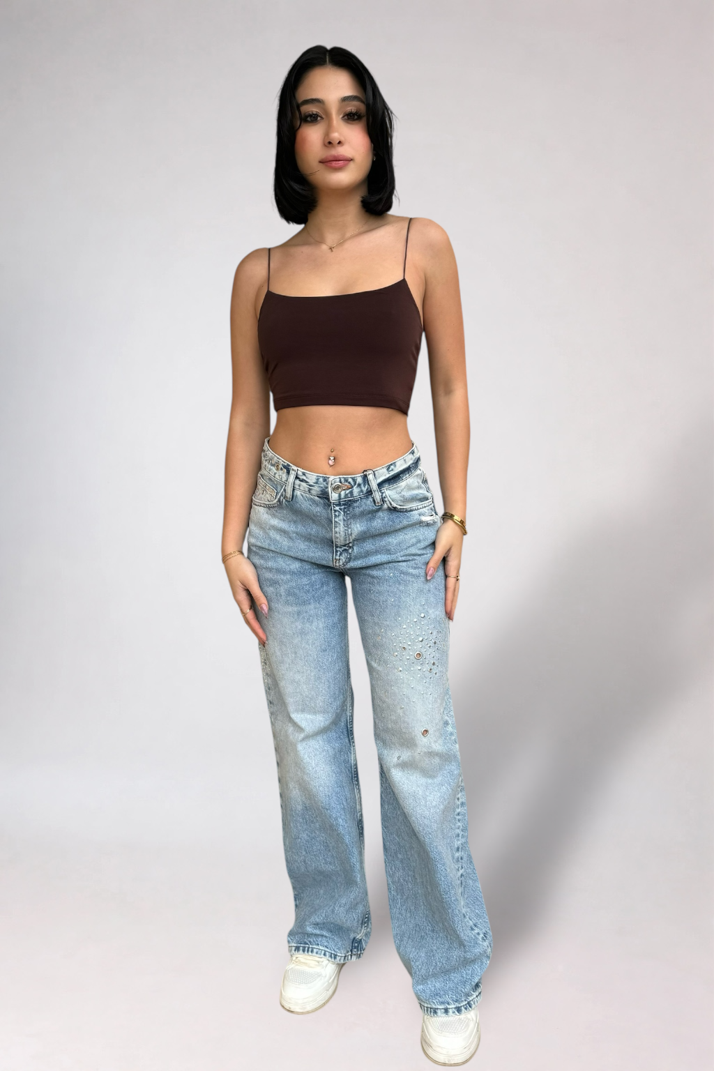 Woman wearing a brown top and blue jeans against a plain background