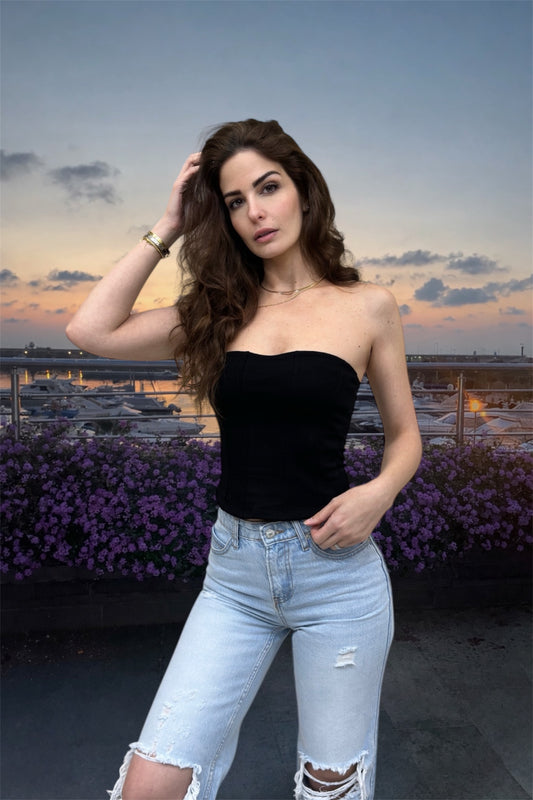 Woman in black top and light blue jeans standing on a rooftop with a cityscape background